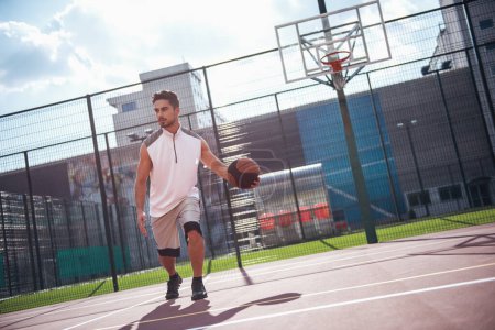 Photo for Handsome basketball player is playing on basketball court outdoors - Royalty Free Image