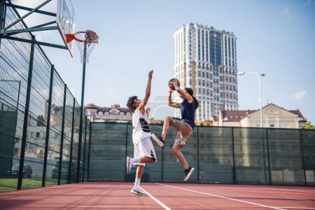 Téléchargez les photos : Beaux joueurs de basket-ball jouent sur le terrain de basket en plein air - en image libre de droit