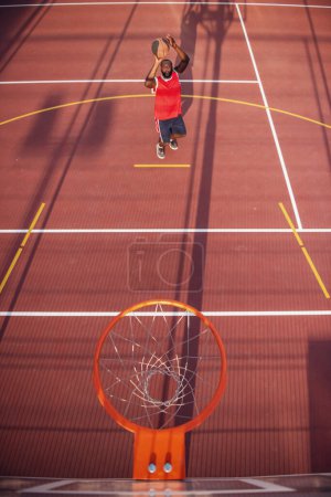 Photo for Top view of handsome basketball player shooting a ball through the hoop while playing on basketball court outdoors - Royalty Free Image