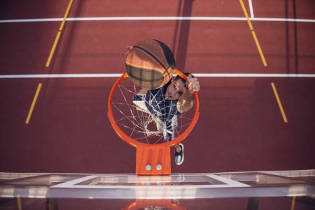 Téléchargez les photos : Vue du dessus du beau joueur de basket tirant une balle à travers le cerceau tout en jouant sur le terrain de basket à l'extérieur - en image libre de droit