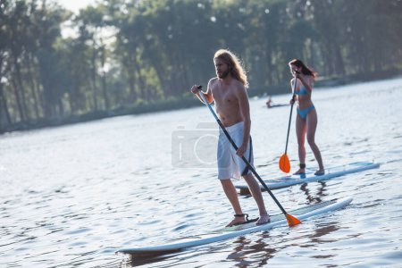 Téléchargez les photos : Beau jeune couple est SUP surf sur la rivière, le soleil se couche - en image libre de droit