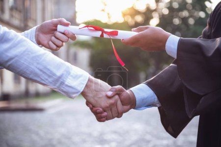 Photo for Cropped image of graduate in academic dress taking his diplomas and shaking hand - Royalty Free Image