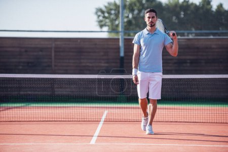 Téléchargez les photos : Beau homme tient raquette de tennis tout en jouant au tennis sur le court à l'extérieur - en image libre de droit