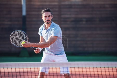 Téléchargez les photos : Beau homme joue au tennis sur le court de tennis en plein air - en image libre de droit