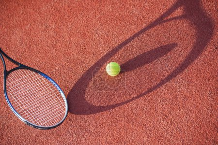 Photo for Small yellow tennis ball is lying on tennis court outdoors, someone is holding a tennis racket near it, weather is sunny - Royalty Free Image