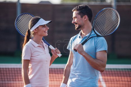 Foto de Hombre guapo y mujer hermosa se miran y sonríen mientras juegan al tenis en la cancha de tenis al aire libre - Imagen libre de derechos
