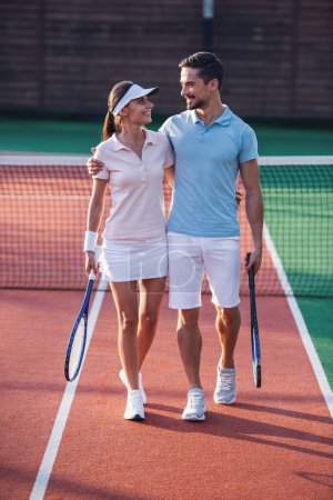Foto de Hombre guapo y mujer hermosa están abrazando y sonriendo mientras están de pie en la cancha de tenis al aire libre después del juego - Imagen libre de derechos