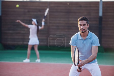 Photo for Beautiful young couple are playing tennis as a team on tennis court outdoors - Royalty Free Image