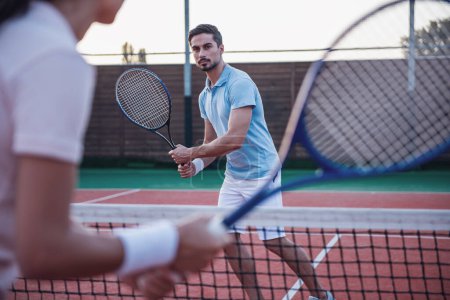 Photo for Beautiful young woman and handsome man are playing tennis on tennis court outdoors - Royalty Free Image