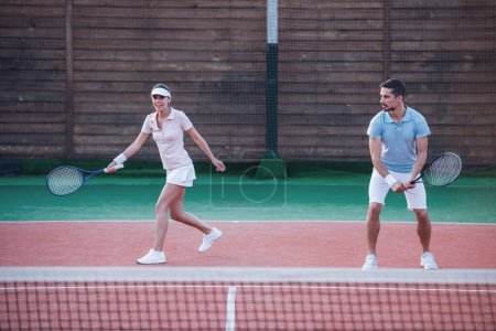 Téléchargez les photos : Beau jeune couple jouent au tennis en équipe sur le terrain de tennis en plein air - en image libre de droit