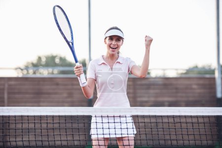 Photo for Beautiful young woman is smiling while playing tennis on tennis court outdoors - Royalty Free Image
