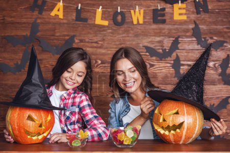 Photo for Cute little girl and her beautiful mom are smiling while preparing pumpkins for Halloween - Royalty Free Image