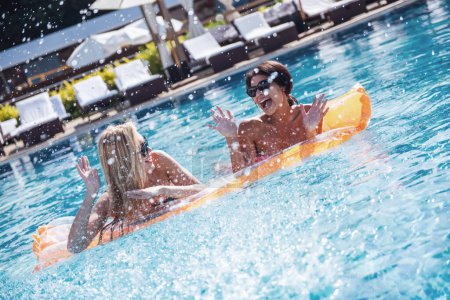Téléchargez les photos : De belles filles dans des lunettes de soleil éclaboussent d'eau et rient tout en étant allongées sur un matelas de piscine - en image libre de droit