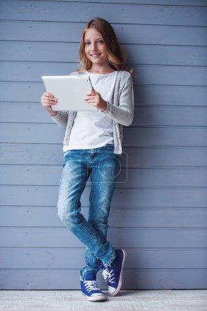 Foto de Bastante adolescente está utilizando una tableta digital y sonriendo mientras - Imagen libre de derechos