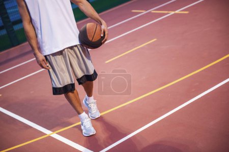 Téléchargez les photos : Image recadrée d'un beau joueur de basket debout avec une balle sur le terrain de basket à l'extérieur - en image libre de droit