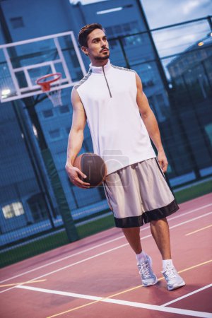 Photo for Full length portrait of handsome basketball player standing with a ball on basketball court outdoors - Royalty Free Image