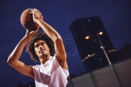 Téléchargez les photos : Joueur de basket attrayant joue au basket en plein air dans la soirée - en image libre de droit