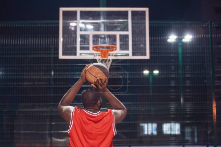 Téléchargez les photos : Beau joueur de basket-ball joue au basket en plein air dans la soirée - en image libre de droit