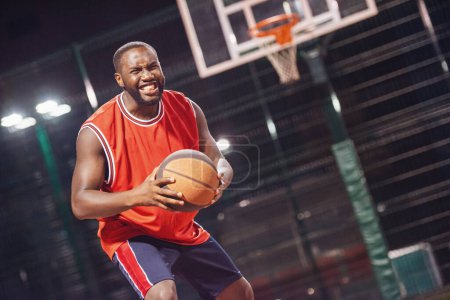 Téléchargez les photos : Beau joueur de basket-ball joue au basket en plein air dans la soirée - en image libre de droit