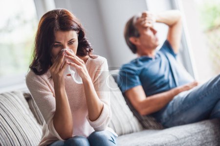 Photo for Couple of adults are quarreling while sitting on couch at home, woman is wiping her tears - Royalty Free Image