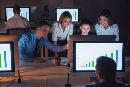 Téléchargez les photos : Les gens d'affaires qui réussissent utilisent un ordinateur et sourient en travaillant au bureau tard dans la nuit - en image libre de droit