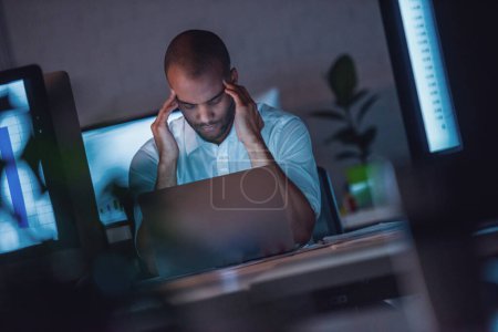 Téléchargez les photos : L'homme d'affaires afro-américain fatigué se masse les tempes en travaillant avec un ordinateur portable au bureau tard dans la nuit - en image libre de droit