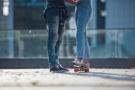 Photo for Cropped image of stylish young couple spending time together in the city. Guy is teaching his girl skateboarding - Royalty Free Image