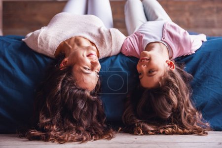 Photo for Beautiful mom and daughter are looking at each other and smiling while lying on their backs on bed at home - Royalty Free Image