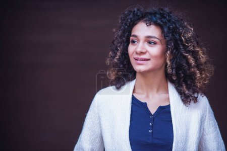 Foto de Retrato de una chica atractiva, mirando hacia un lado y sonriendo, sobre el fondo de una pared marrón - Imagen libre de derechos