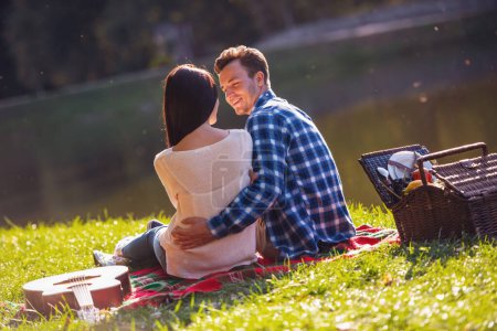 Téléchargez les photos : Vue de dos de beau jeune couple parlant et se câlinant tout en se reposant sur un plaid dans le parc - en image libre de droit