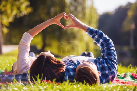 Photo for Back view of beautiful young couple making a heart while lying on a plaid in the park - Royalty Free Image