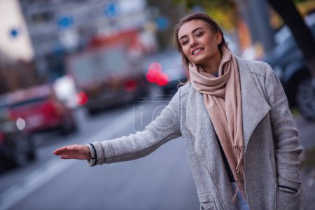 Téléchargez les photos : Belle fille en manteau sourit et lève les mains tout en attrapant un taxi dans la ville - en image libre de droit
