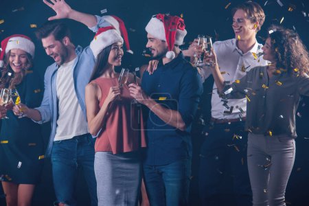 Téléchargez les photos : Groupe heureux de personnes buvant du champagne, acclamant et souriant tout en célébrant le Nouvel An, sur fond sombre et fumé - en image libre de droit