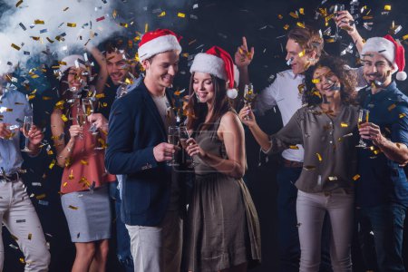Photo for Happy people drinking champagne and having fun while celebrating New Year, on dark smoky background. Beautiful couple in the foreground - Royalty Free Image