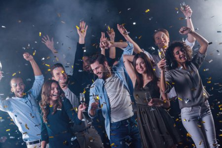 Téléchargez les photos : Heureux groupe de personnes buvant du champagne, dansant et souriant tout en célébrant le Nouvel An, sur fond sombre et fumé - en image libre de droit