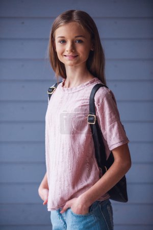 Foto de Atractiva adolescente con mochila mirando a la cámara y sonriendo contra el fondo de la pared de madera - Imagen libre de derechos