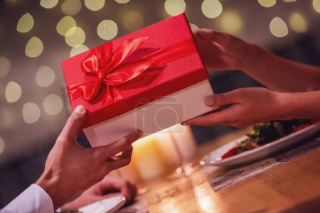 Foto de Imagen recortada de una joven pareja sosteniendo una caja de regalo mientras celebra el Año Nuevo en un restaurante - Imagen libre de derechos