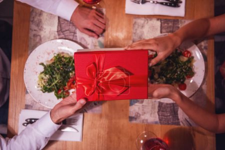 Foto de Imagen recortada de una joven pareja sosteniendo una caja de regalo mientras celebra el Año Nuevo en un restaurante, vista superior - Imagen libre de derechos