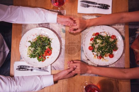 Téléchargez les photos : Cropped image de jeune couple tenant la main pendant leur date dans un restaurant, vue du dessus - en image libre de droit