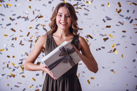 Photo for Attractive young woman in dress is holding presents, looking at camera and smiling, on light background - Royalty Free Image