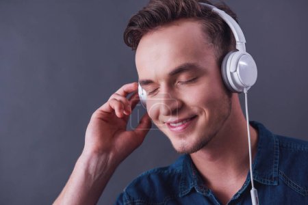 Photo for Handsome young man in headphones is listening to music, on gray background - Royalty Free Image