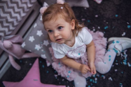 Téléchargez les photos : Petite fille mignonne joue avec des confettis dans la chambre des enfants - en image libre de droit