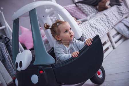 Téléchargez les photos : Petite fille mignonne joue avec une voiture jouet dans la chambre des enfants - en image libre de droit