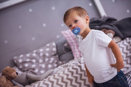 Photo for Cute little boy with a pacifier is standing in the children's room - Royalty Free Image
