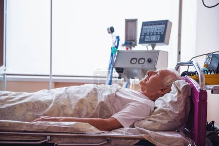 Téléchargez les photos : Un vieil homme couché les yeux fermés dans une chambre d'hôpital. - en image libre de droit