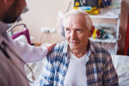 Téléchargez les photos : Beau vieil homme parle avec un médecin alors qu'il est assis dans la salle d'hôpital - en image libre de droit