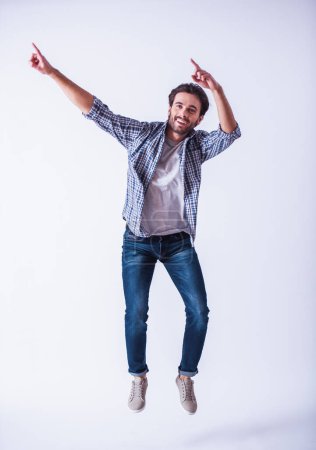 Foto de Hombre barbudo guapo con ropa casual está apuntando, saltando y sonriendo, sobre un fondo claro - Imagen libre de derechos