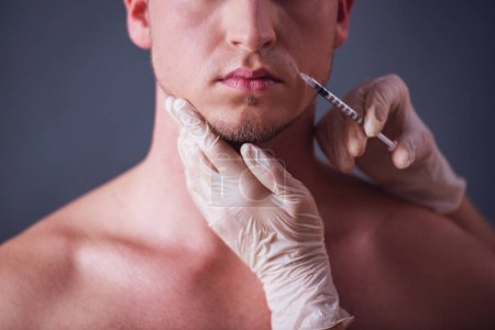 Photo for Cropped image of handsome young man getting face injection, on gray background - Royalty Free Image
