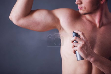 Téléchargez les photos : Image recadrée de beau jeune homme avec torse nu à l'aide d'antitranspirant, sur fond gris - en image libre de droit