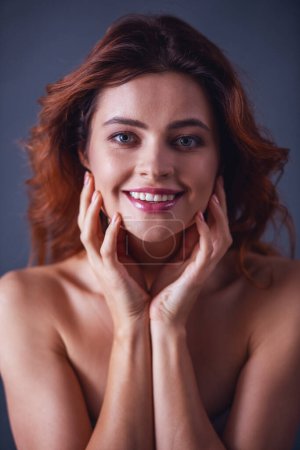 Foto de Retrato de una joven mujer hermosa con hombros desnudos sobre un fondo gris y una sonrisa a la cámara - Imagen libre de derechos